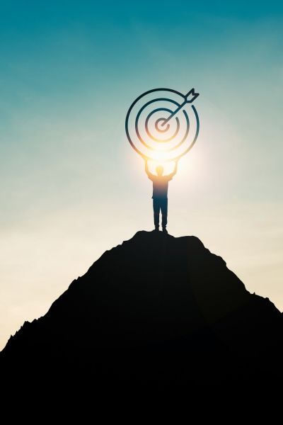 Silhouette of businessman holding target board on the top of mountain with over blue sky and sunlight. It is symbol of leadership successful achievement with goal and objective target. Silhouette of businessman holding target board on the top of mountain with over blue sky and sunlight. It is symbol of leadership successful achievement with goal and objective target.